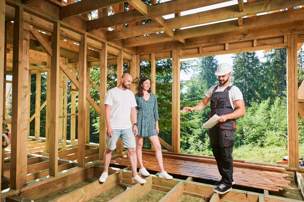 Construction worker discussing plans with a couple at a wooden house frame construction site.